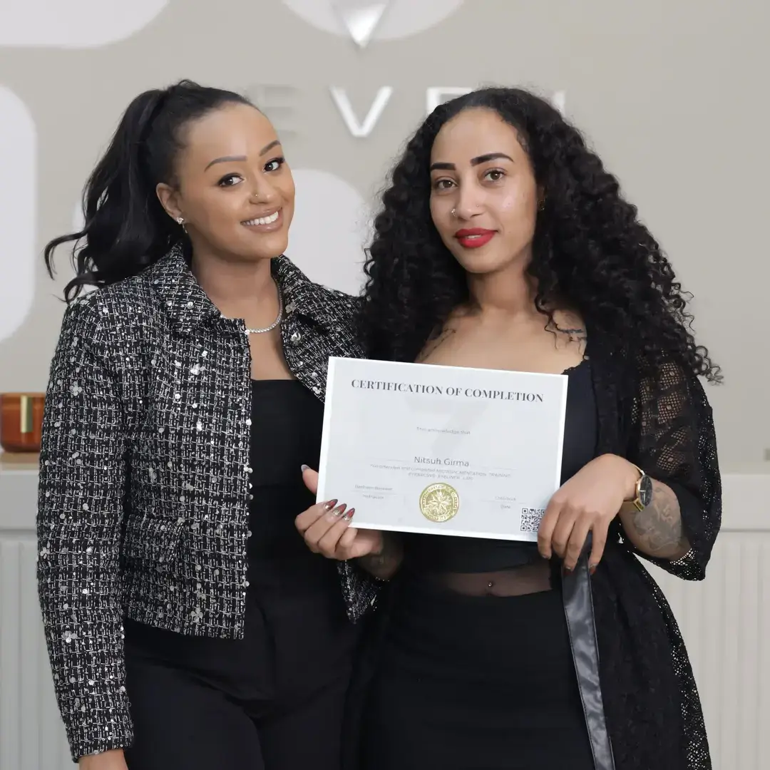 Permanent Makeup Certification at Seven Aesthetics: Teacher Betlehem Bereket with student Mihiret Girma holding her certificate of completion after completing the course.